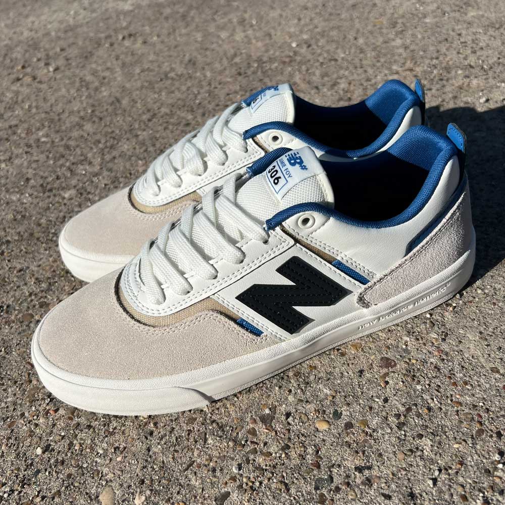 A pair of 306 TWC Jamie Foy New Balance Numeric Suede Shoes in white, blue, black, and brown sits on a textured concrete surface in sunlight.