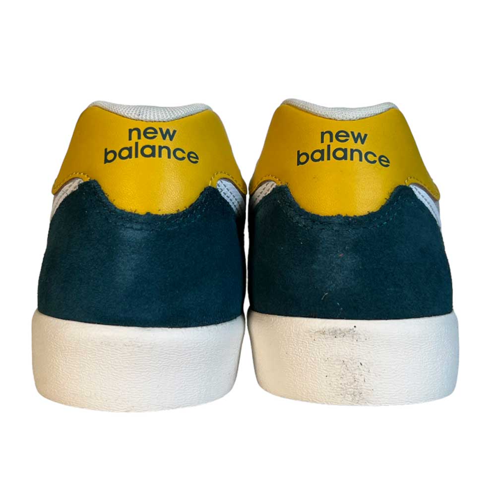 A pair of 574 VOK New Balance Numeric Gray White Suede Shoes seen from the back, featuring yellow heel tabs, dark green suede accents, white midsoles, and minor wear on the right sole—ideal skate shoes with signature New Balance style.