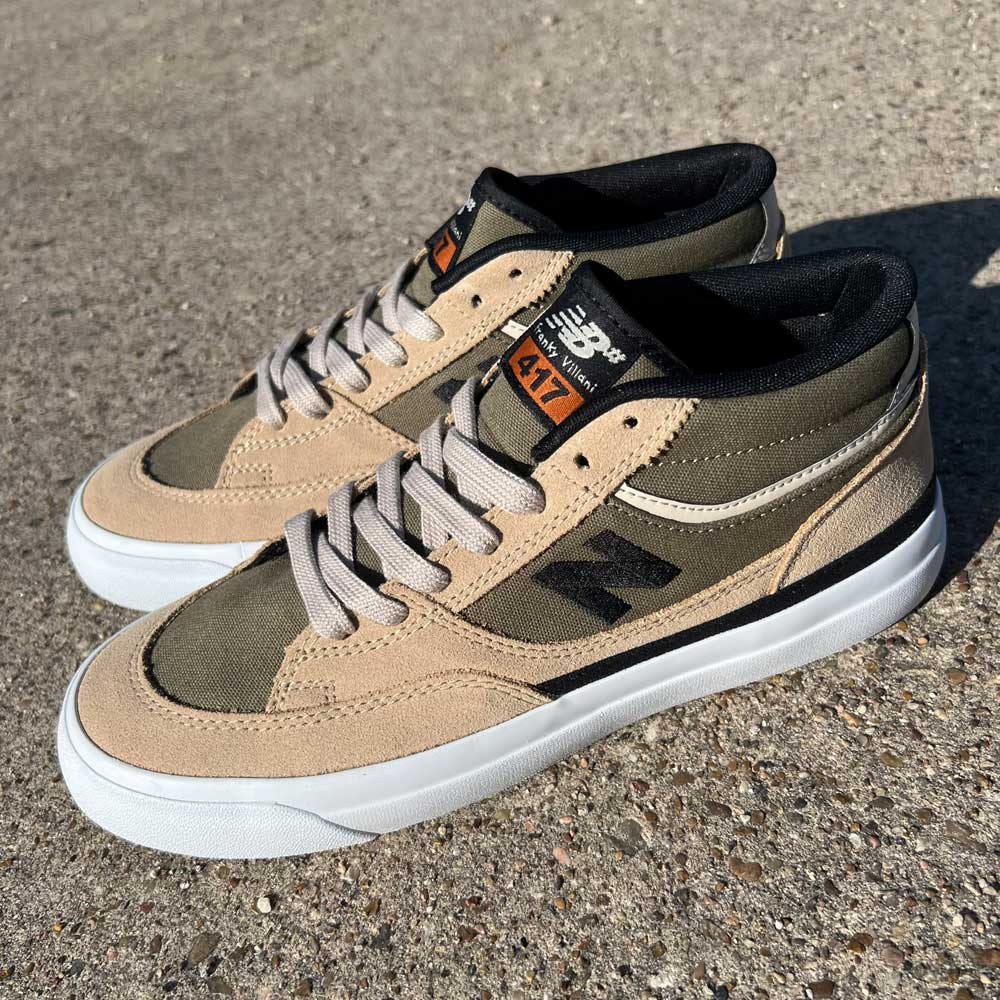 A pair of 417 FFU Franky Villani New Balance Numeric suede shoes in tan, olive, white, and black are shown on a rough outdoor concrete surface in sunlight.