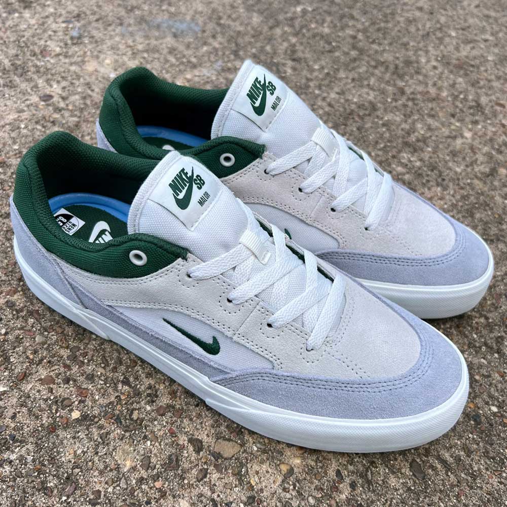 The FV6064002 Platnium Fir Wolf Gray White Suede Nike SB Shoes feature light grey and white tones with dark green accents, suede canvas details, and Nike logos, shown on a rough concrete surface.
