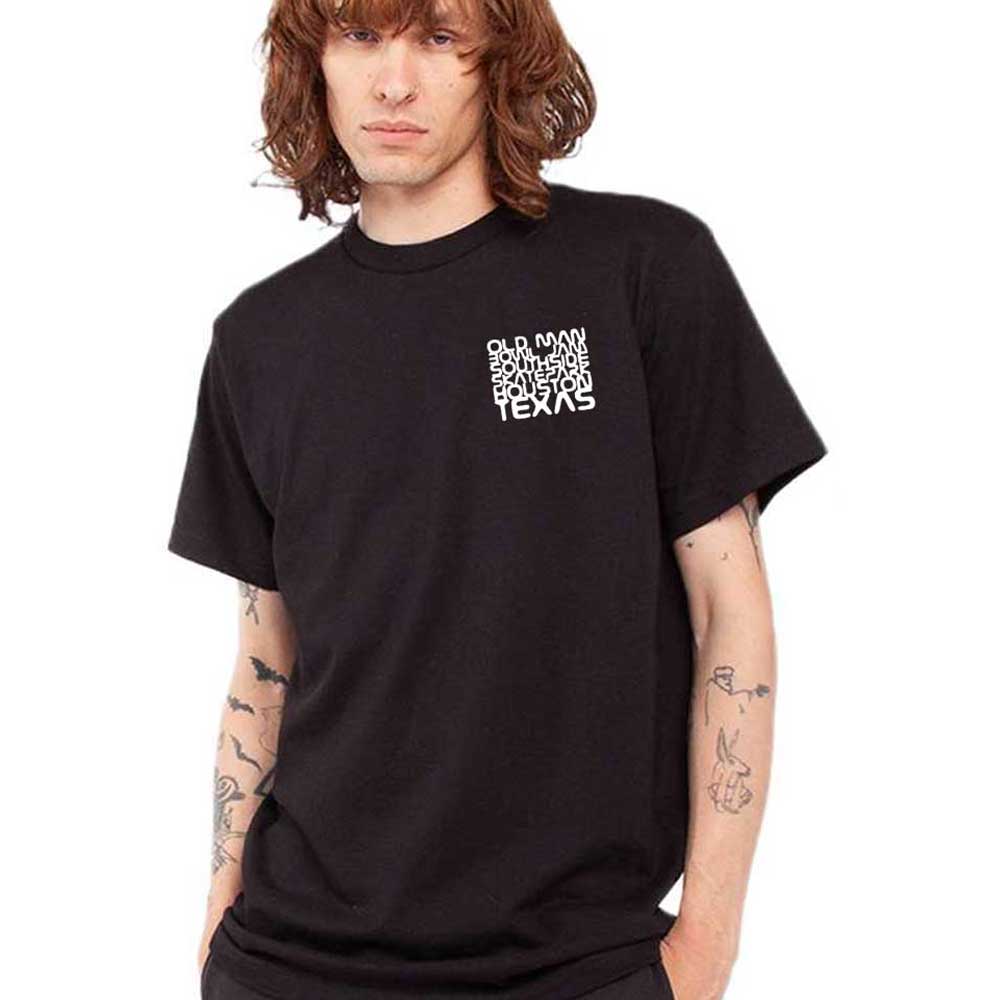 A person with wavy, shoulder-length hair and arm tattoos stands with a neutral expression in a black Pre-Order Old Man Bowl Jam 2026 T-Shirt at Southside Skatepark, ready for the event.