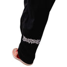 A close-up of a lower leg wearing Texas Icon Black Southside 94 Pants with jagged white text near the ankle and red-and-white shoes, highlighting the loose-fit skate style favored in Southside skateboarding.