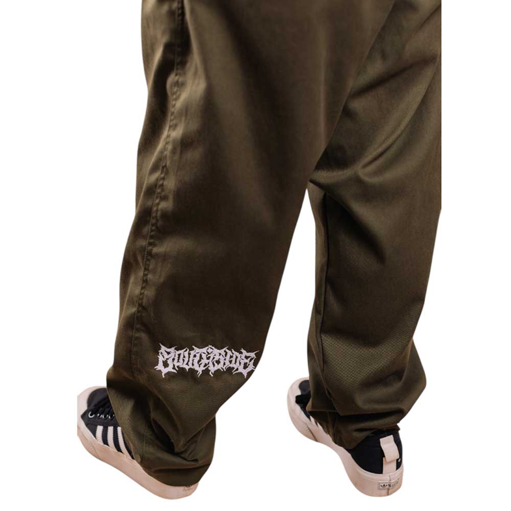 Someone wearing loose-fitting Texas Icon Dark Green Southside 94 Pants with a white graphic near the left ankle, paired with black and white sneakers, stands on a white background.