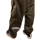 Someone wearing loose-fitting Texas Icon Dark Green Southside 94 Pants with a white graphic near the left ankle, paired with black and white sneakers, stands on a white background.