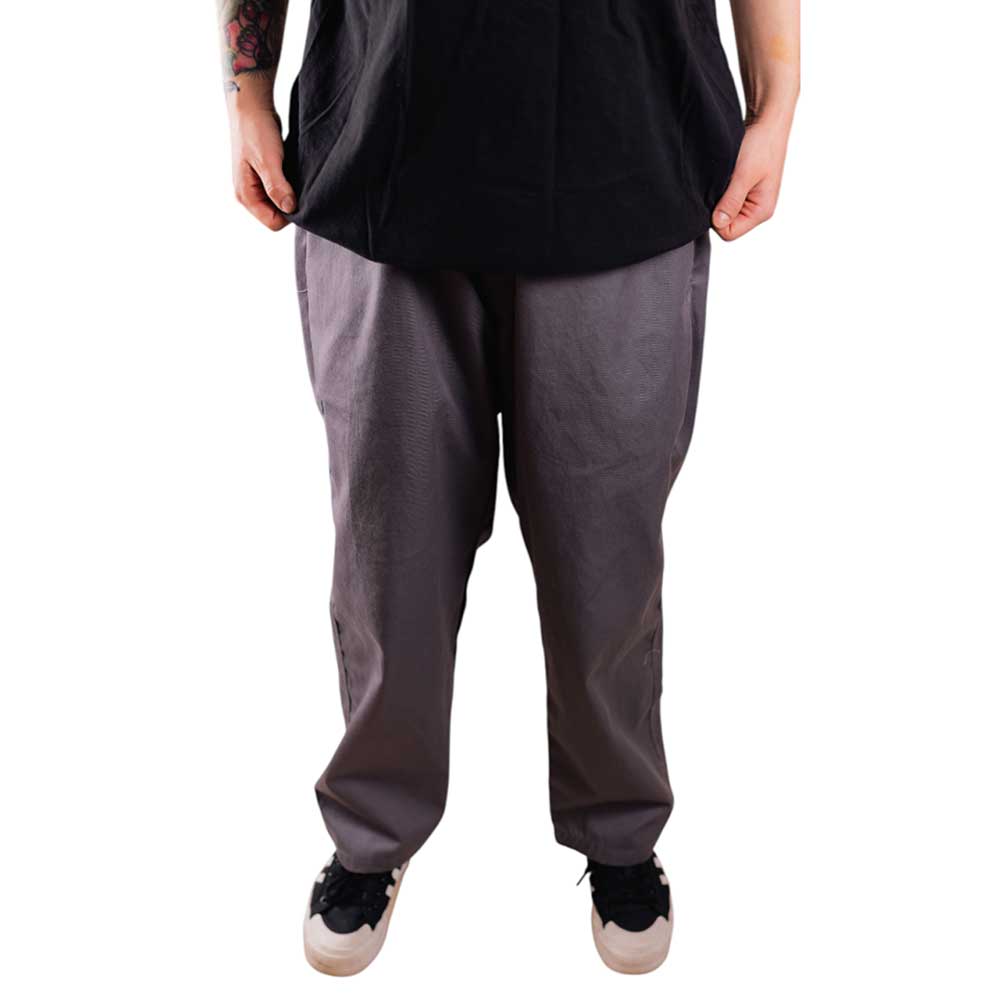 Only the lower half is visible against a white background, with the model standing hands by their sides, wearing gray Texas Icon Southside 94 Pants—loose-fitting and rugged—paired with a black shirt and black sneakers with white soles.