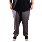 Only the lower half is visible against a white background, with the model standing hands by their sides, wearing gray Texas Icon Southside 94 Pants—loose-fitting and rugged—paired with a black shirt and black sneakers with white soles.