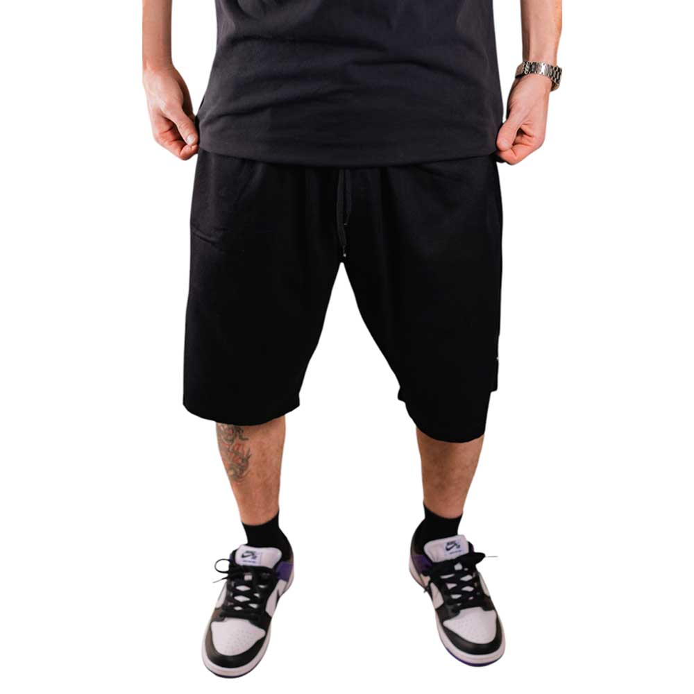 Wearing Texas Icon Black Southside 94 Shorts, black and white sneakers, a wristwatch, and a black T-shirt, a person stands against a white background with only the lower half of their body visible.