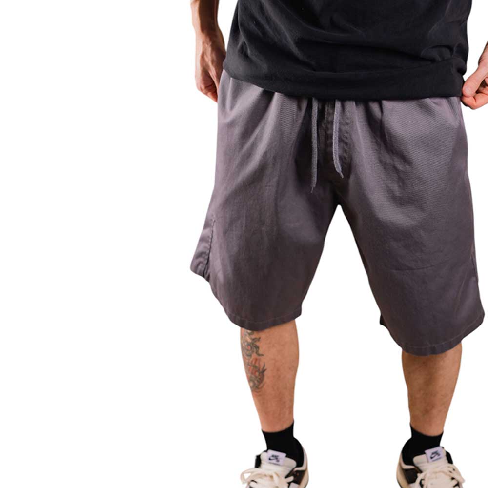 Wearing Texas Icon Gray Southside 94 Shorts, black T-shirt, black socks, and white sneakers, only the lower half is visible, showing a leg tattoo on a white background. These shorts are perfect for bold, casual skateboarding style.