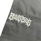 A close-up of Texas Icon Gray Southside 94 Pants fabric, showing white spiky gothic-style embroidered text that reads “Delicious.”.