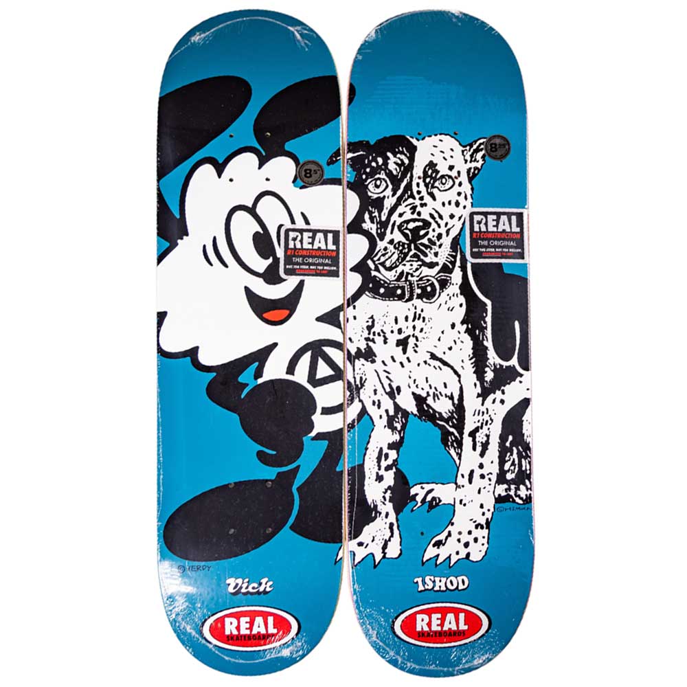 Two Verdy Vick 8.5 Real Skateboard Decks with blue backgrounds: the left shows a cartoon hand, the right features a black and white dog. Both display REAL logos at the bottom—part of the Skateshop Day collection.