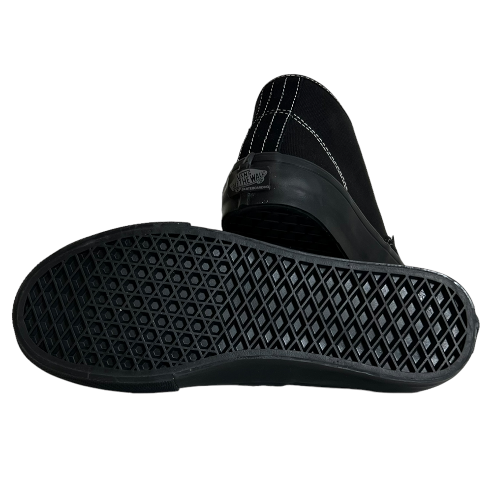 The VN0A27371OJ Suede Black Authentic Mid Vans Skate Shoes are slip-ons, with one shoe upright and the other showing a textured waffle-patterned sole; white stitching accents the back, emphasizing their durability.