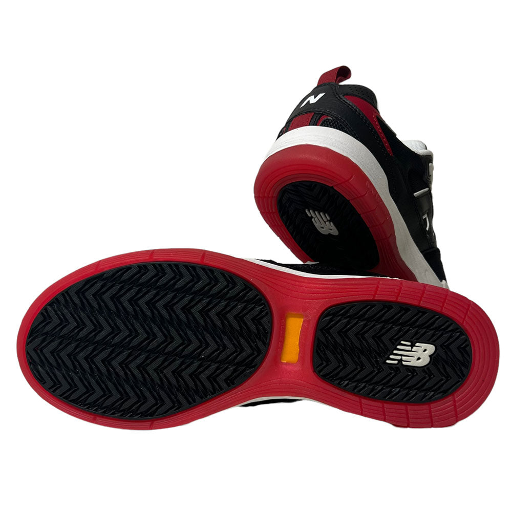 The New Balance NM 808 Tiago Black Red White sneakers are shown, with one upright and the other displaying its black sole with red edges, tread pattern, and white NB logo—a highlight of Tiago’s signature collection.