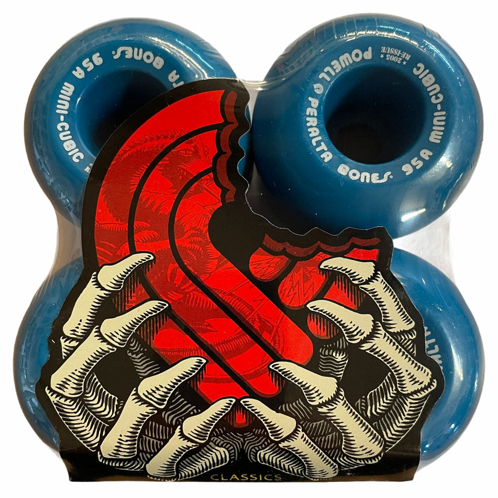 Four Powell Peralta Wheels Mini Cubic 64mm95A Blue are packaged together, partially covered by artwork of skeletal hands holding a red S-shaped bitten tongue. "Powell Peralta Bones 95A Mini-Cubic" is printed in white on the wheels.