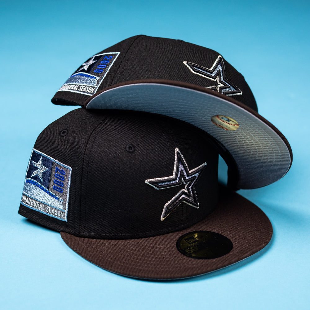 Two black The Magician Houston Astros New Era 5950 Fitted hats with star logos and Inaugural Season 2002 patches are stacked on a blue surface. One hat is tilted to display its light gray undervisor—making it a perfect Whatafitted pick for Houston Astros fans.