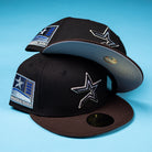 Two black The Magician Houston Astros New Era 5950 Fitted hats with star logos and Inaugural Season 2002 patches are stacked on a blue surface. One hat is tilted to display its light gray undervisor—making it a perfect Whatafitted pick for Houston Astros fans.