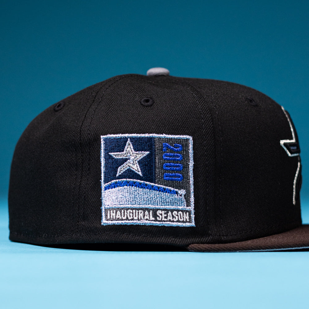 The Magician Houston Astros New Era Hat 5950 Fitted is a black baseball cap featuring a star patch with “2000” and “Inaugural Season” on the side, honoring the Houston Astros, displayed against a blue background.