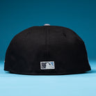 A black The Magician Houston Astros New Era Hat 5950 Fitted is placed on a blue surface, viewed from the back, displaying a small rectangular white and blue logo near the bottom edge.