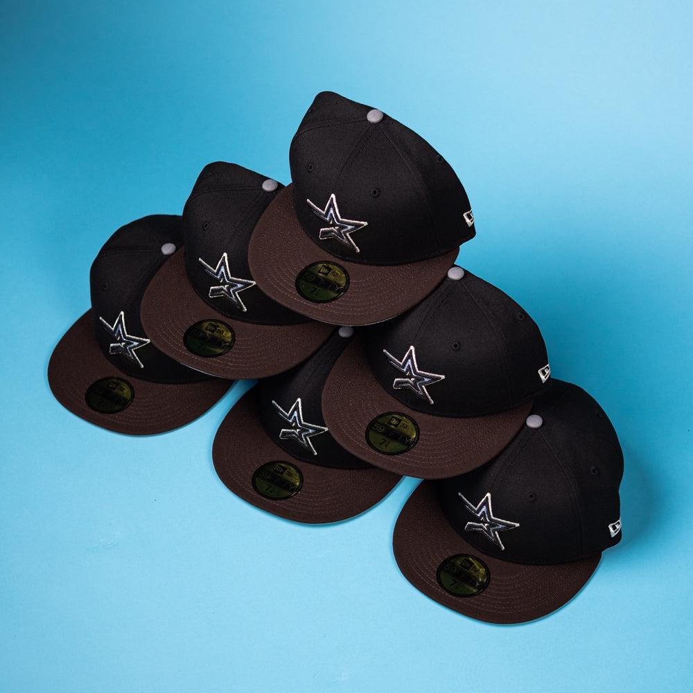 Six black and brown “The Magician Houston Astros New Era Hat 5950 Fitted” baseball caps featuring star logos are arranged in a pyramid shape on a blue background.