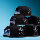 Five black “The Magician Houston Astros New Era Hat 5950 Fitted” caps, featuring a silver star emblem and a blue 2001 Inaugural Season patch, are neatly stacked against a blue background. Offered by Whatafitted and crafted by New Era, these stylish hats blend sleek design with iconic team pride.