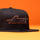 A BLVCK STAR Houston Astros New Era Hat 5950 Fitted in black, featuring “Houston Astros” embroidered in bold black and copper lettering on the front, shown against an orange background.