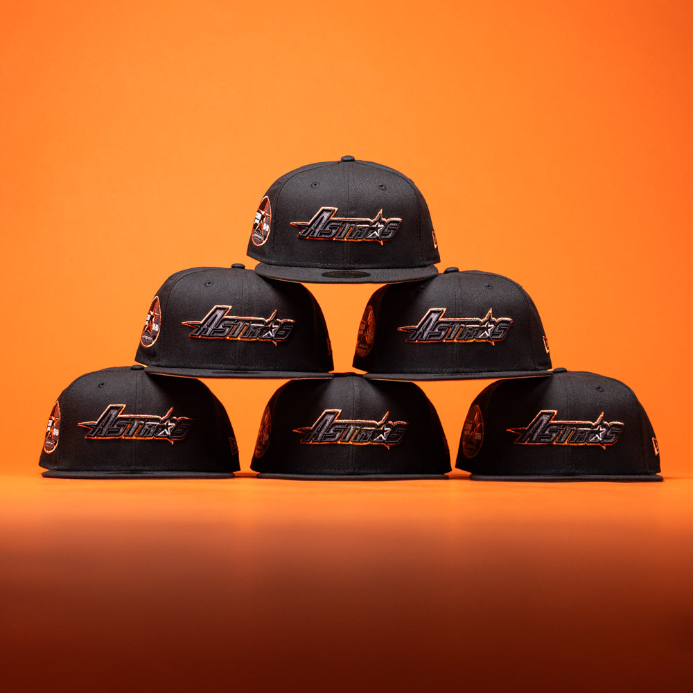 Six BLVCK STAR Houston Astros New Era Hat 5950 Fitted caps are arranged in a pyramid on an orange background.