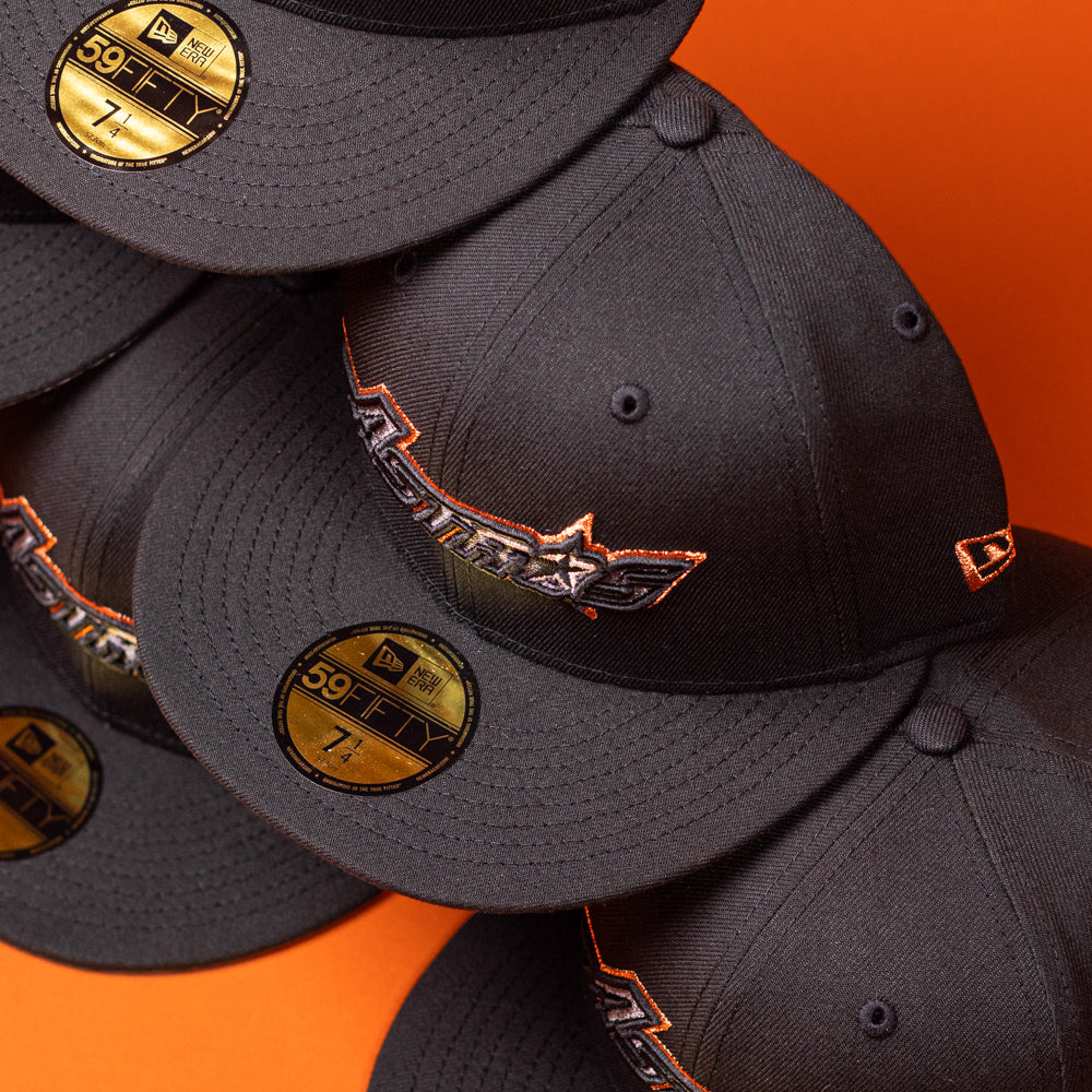 Five BLVCK STAR Houston Astros New Era 59FIFTY fitted hats are stacked against an orange background, with gold 59FIFTY stickers visible on the brims and the Astros logo embroidered on the front of each cap in a striking Black Copper finish.