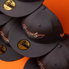 Five BLVCK STAR Houston Astros New Era 59FIFTY fitted hats are stacked against an orange background, with gold 59FIFTY stickers visible on the brims and the Astros logo embroidered on the front of each cap in a striking Black Copper finish.