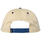 Back view of the 3rd and Army Natural Navy Real Skateboards Hat Adjustable, featuring a beige design with a blue adjustable snap closure and two dark eyelets on top. A small tag with "REAL" is attached near the closure, reflecting its authentic style inspired by 3rd and Army.