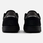 Rear view of a pair of durable black 440 BVU New Balance Numeric Suede Skateboarding Shoes, featuring perforated details and metallic silver New Balance branding on the heels, equipped with an ABZORB midsole for superior cushioning, set against a plain white background.
