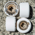 Four 54mm Double Duro Gum Chubbies 101a 95a OJ Wheels are arranged in a square on rough concrete. Two wheels show black and gold OJ graphics, while the other two display plain white sides.