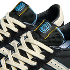 Close-up of Thrasher Magazine Glenburn Black Blue KH7384 Adidas Skateboarding Shoes featuring off-white laces, blue accents, a blue and yellow tongue logo patch, textured fabric tongue, stitched side stripe, and classic adidas trainers vibe.