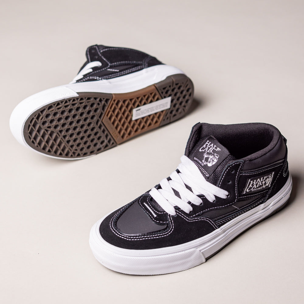 The Vans Wafflecup Half Cab Black White VN000D9ZBA2 Suede Skate Shoes feature black and white suede uppers, white laces, graphic side designs, and thick WaffleCup soles, shown on a light beige surface.