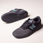 A pair of Black Cement New Spruce 508 TAC New Balance Numeric Suede Skateboarding Shoes, featuring black and gray tones with teal accents—one upright and one showing the sole—displayed on a plain light surface.