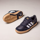 A pair of Black White Gum Tyshawn 2 II HQ4734 Adidas Skateboarding Shoes, featuring white stripes and gum soles, is displayed on a light beige background—one shoe upright and the other showing the sole.