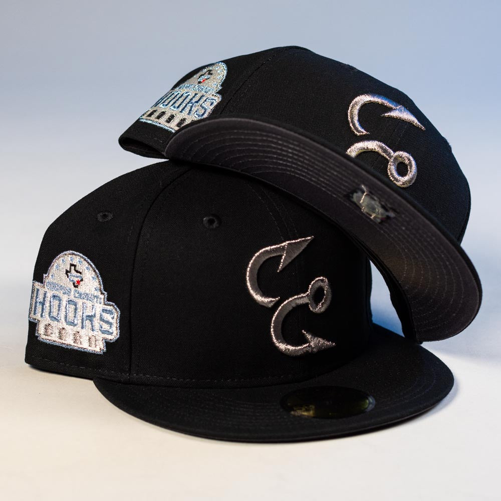Two Eagle Claw Canvas Black Corpus Christi Hooks New Era 5950 Fitted Hats display silver and blue logos. One is upright, showing the front, while the other is tilted to reveal its brim and side patch.