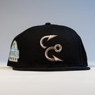 The Eagle Claw Canvas Black Corpus Christi Hooks New Era Hat 5950 Fitted features two metallic silver fishing hook designs on the front and a left-side patch with the Hooks logo.