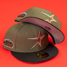 Two "The Original Olive Black CC Astros New Era Hat 5950 Fitted" caps, featuring orange star logos and special event patches, are displayed on a bright red background—one upright and one revealing its brim underside.