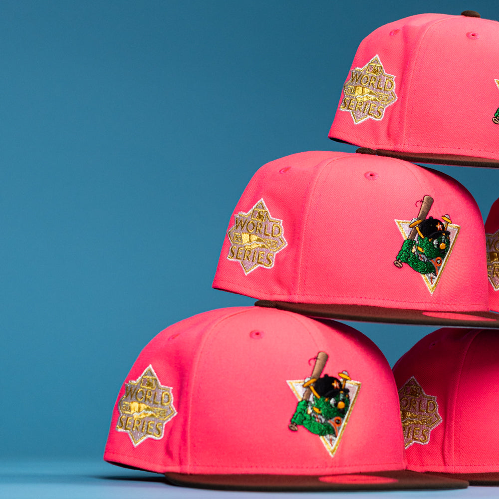 Four Pink Comet WS22 Houston Astros New Era Hat 5950 Fitted caps are stacked in two columns on a blue background, each featuring a gold World Series patch on the side and a colorful parrot with bat logo patch on the front.