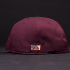 The 05 Debut Maroon Black Houston Astros New Era Hat 5950 Fitted is shown from the back, displaying a small embroidered MLB logo in white, blue, and gold near the bottom edge. The hat sits on a dark surface against a black background.