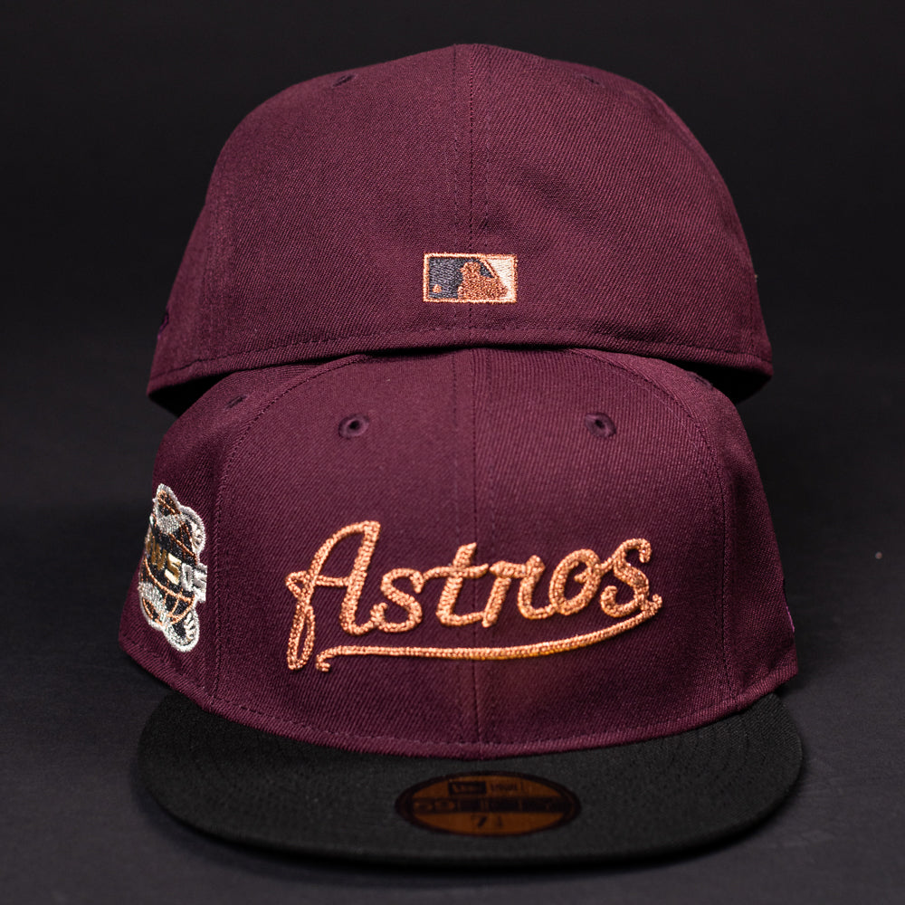 Two maroon 05 Debut Maroon Black Houston Astros New Era 5950 Fitted hats feature black brims; one has gold Houston Astros script and a commemorative patch, while the other shows the MLB logo above the closure, both set against a black background.