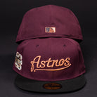 Two maroon 05 Debut Maroon Black Houston Astros New Era 5950 Fitted hats feature black brims; one has gold Houston Astros script and a commemorative patch, while the other shows the MLB logo above the closure, both set against a black background.