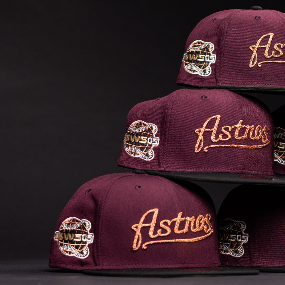 Three 05 Debut Maroon Black Houston Astros New Era Hat 5950 Fitted caps with gold “Astros” embroidery and a black-and-gold 50th anniversary patch are stacked on black shelves against a dark background.