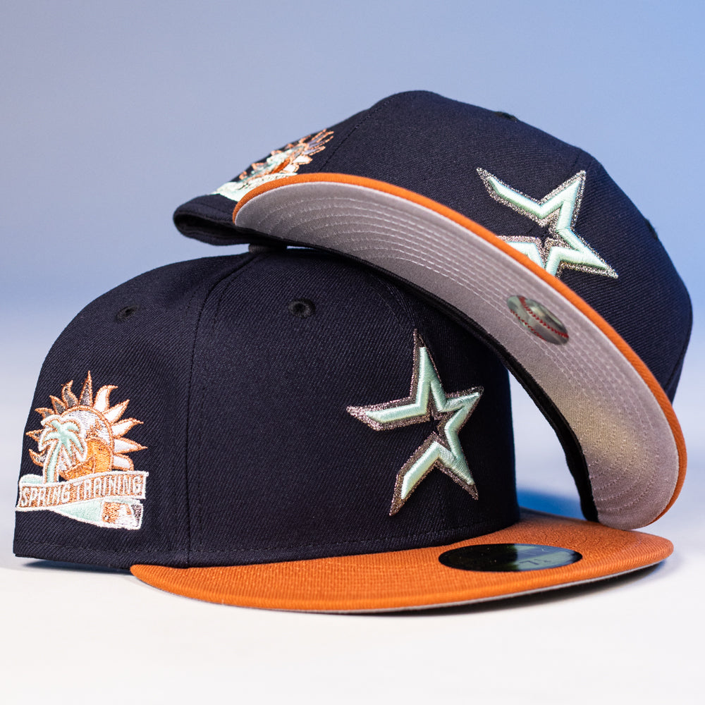 Two Feast Navy Rust Houston Astros New Era 5950 Fitted hats, each with orange brims and silver star logos, stacked together. The caps feature a Spring Training patch with a palm tree and sun on the side.