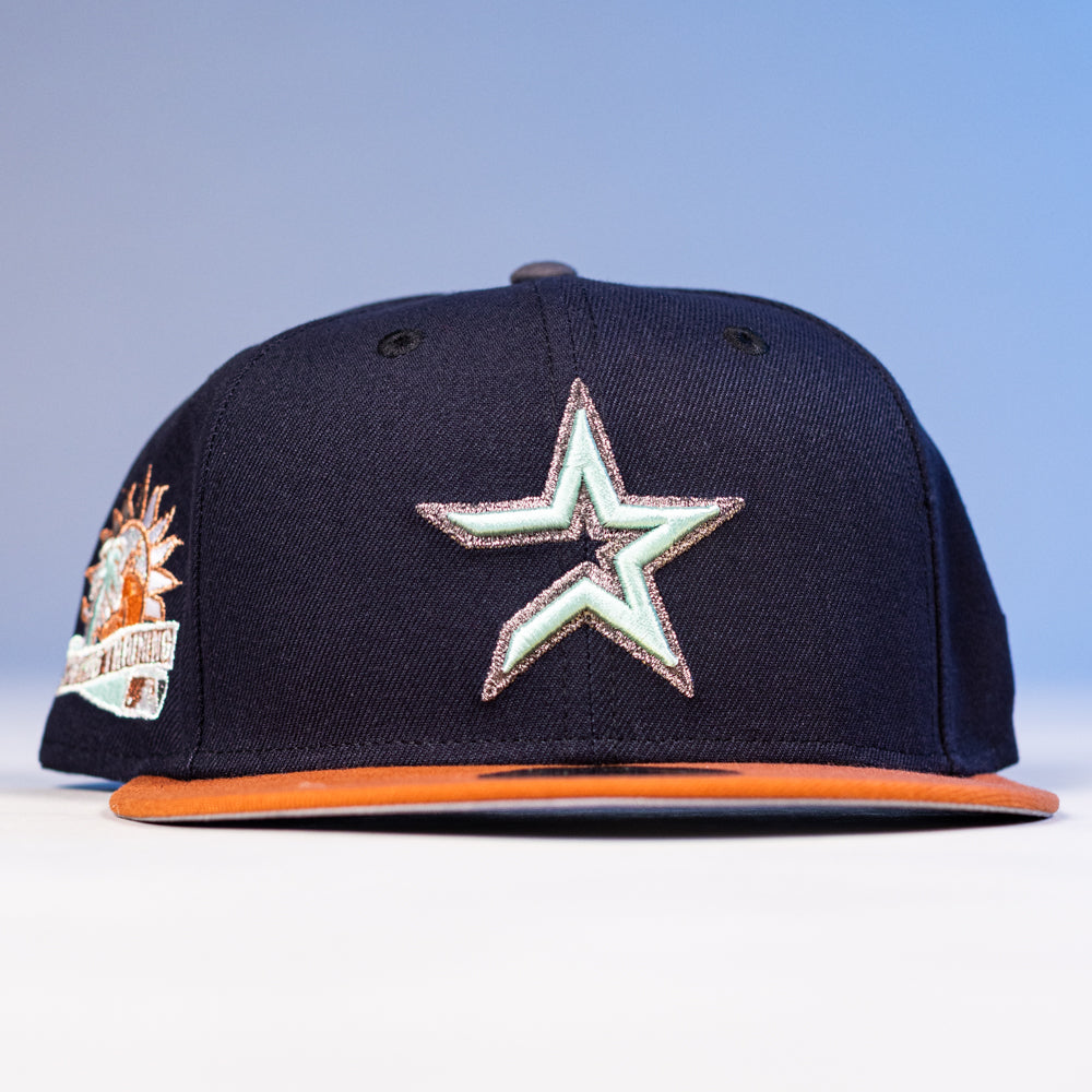 The Feast Navy Rust Houston Astros New Era Hat 5950 Fitted features a navy crown, orange brim, large silver and light blue star front logo, and a colorful embroidered Astros patch on the left side.