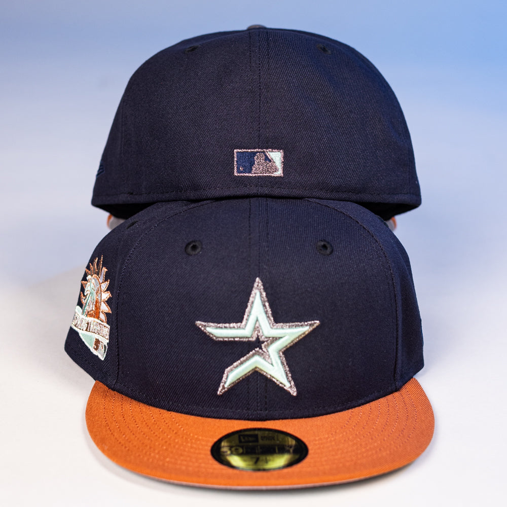 Two The Feast Navy Rust Houston Astros New Era Hat 5950 Fitted caps are stacked, showing the star logo and an orange brim on the front hat, with a Statue of Liberty patch on the side and a small MLB logo on the back cap.