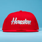 A Cougar Scarlet Houston Cougars New Era 5950 Fitted Hat, featuring "Houston" in white script on the front, is showcased against a light blue background.