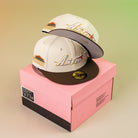 Two cream and brown Oompa Pink Box Houston Astros 5950 Fitted New Era Hats with embroidered logos and patches are stacked on a pink box against a yellow-green gradient background.