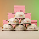 A stack of hats, featuring the Oompa Pink Box Houston Astros New Era Hat 5950 Fitted, with a pink box behind them.