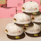 Five cream and brown Oompa Pink Box Houston Astros New Era Hat 5950 Fitted caps are stacked together, each featuring the Astros logo and a 50th anniversary patch. Pink boxes are blurred in the background.