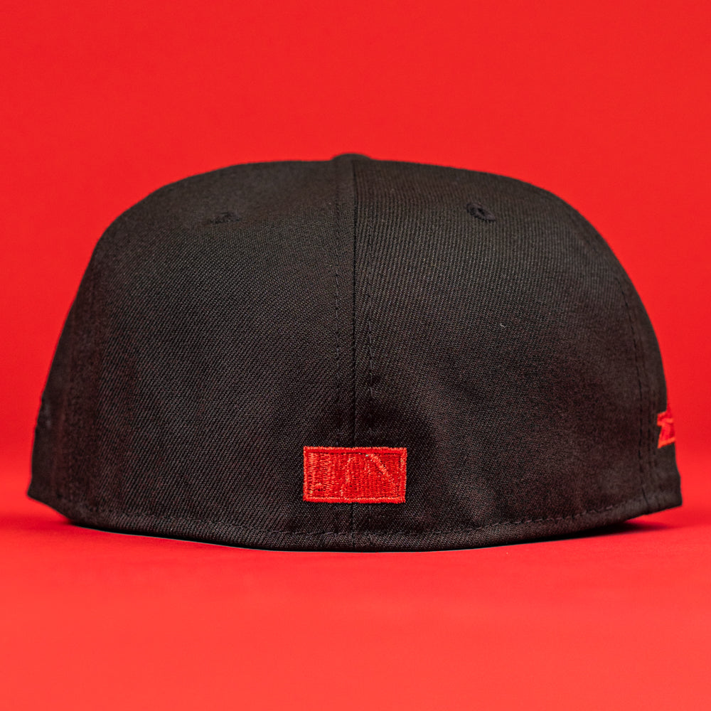 The Shootah Black Silver New Era Hat 5950 Fitted is shown from the back, highlighting a small red embroidered patch on black fabric, all set against a solid red background.